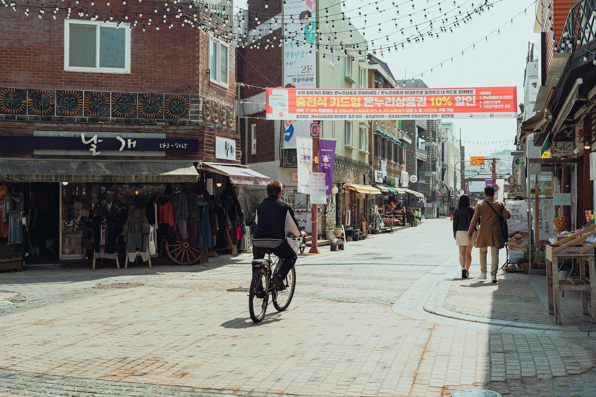 Discover the lively street scene in Suwon-si with local shops and cyclists, capturing the essence of Korean urban life.